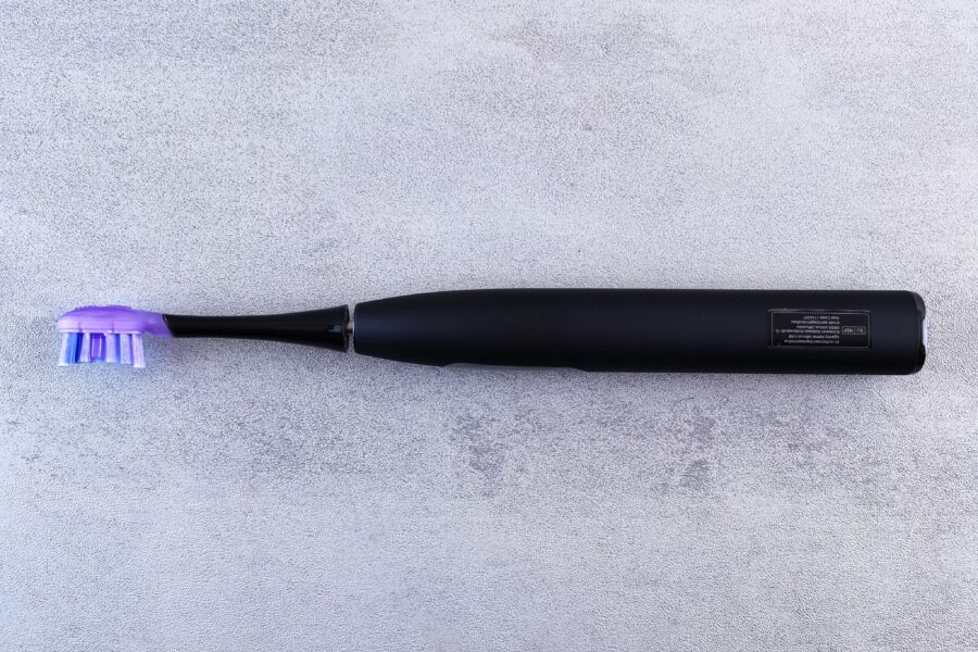Un elegante cepillo de dientes eléctrico negro con una cabeza púrpura descansa sobre una superficie de hormigón texturizado.