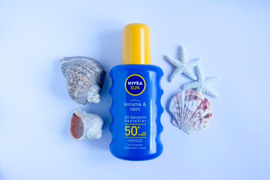 Botella de protector solar Nivea Sun SPF 50+ azul sobre fondo blanco con conchas marinas y estrellas de mar para el cuidado de la piel en verano.