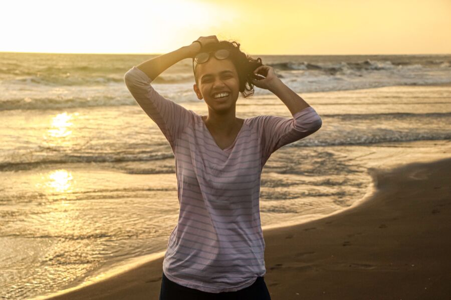 Una mujer sonriente disfrutando del atardecer en una playa de la India, creando un momento cálido y alegre.
