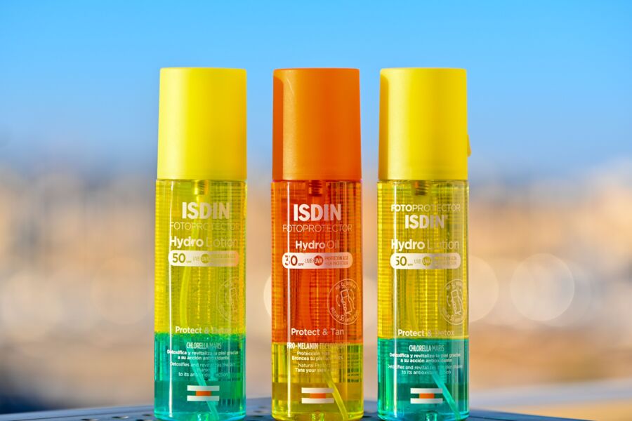 Tres coloridas botellas de protección solar ISDIN contra un fondo borroso, que muestran un embalaje vibrante.
