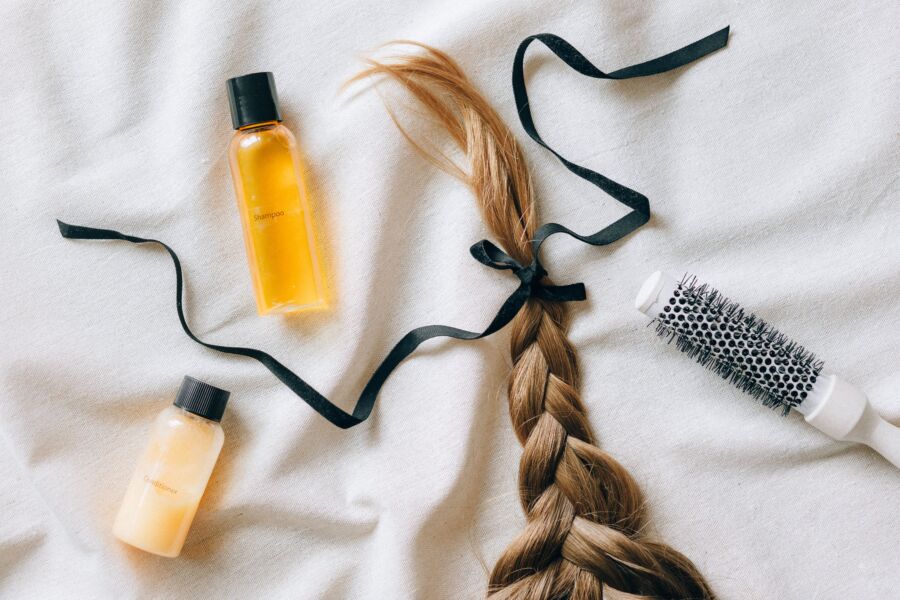 Tejido plano de cabello trenzado con botellas de champú y pincel sobre tela blanca, transmitiendo temas de belleza y cuidado del cabello.