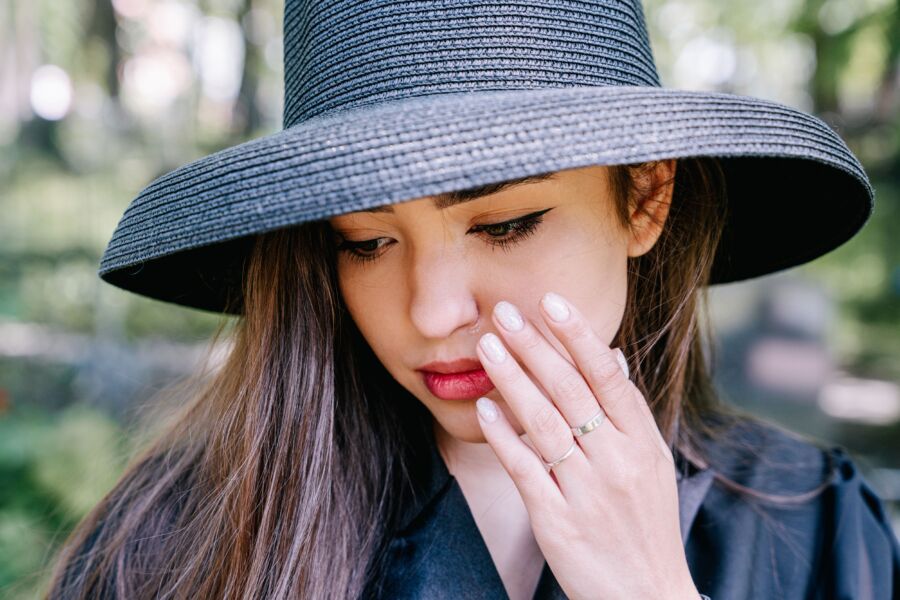 Una mujer pensativa con un sombrero negro con la mano a la cara, al aire libre.