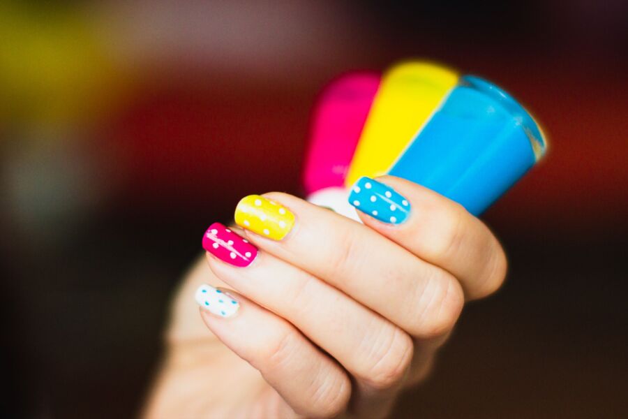 Primer plano de una mano con un colorido arte de uñas a lunares que sostiene vibrantes botellas de esmalte de uñas.