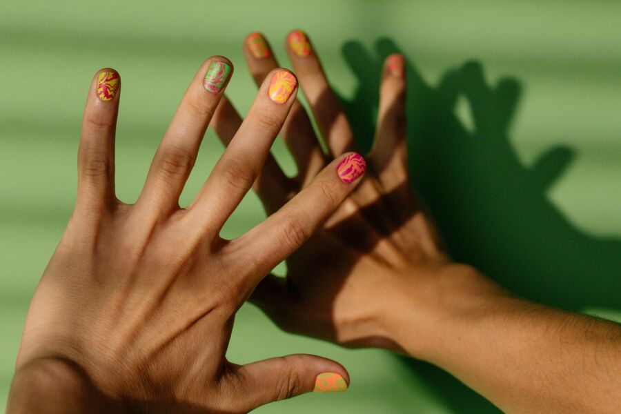Arte de uñas vibrante en las manos proyectando sombras sobre un fondo verde brillante.