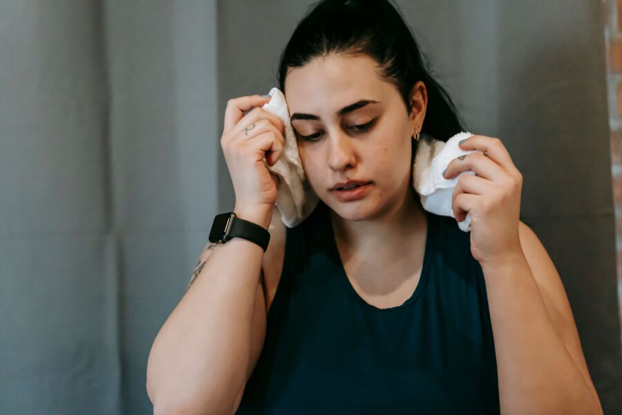 Sobrepeso agotado mujer étnica con cabello negro en ropa deportiva limpiando el sudor de la cara mirando hacia abajo mientras entrena en un gimnasio moderno