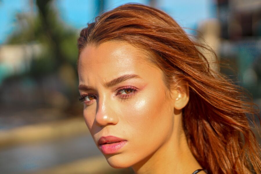 Joven pensativa mujer étnica con cabello de jengibre y piel perfecta y brillante descansando en la playa en un día soleado y mirando a la cámara