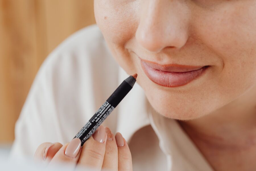 Imagen en primer plano de una mujer aplicando delineador de labios con precisión, destacando la belleza y el autocuidado.