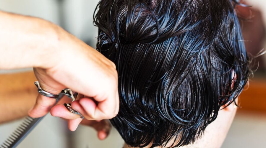 Primer plano de un peluquero cortando el pelo mojado oscuro con unas tijeras en una peluquería.