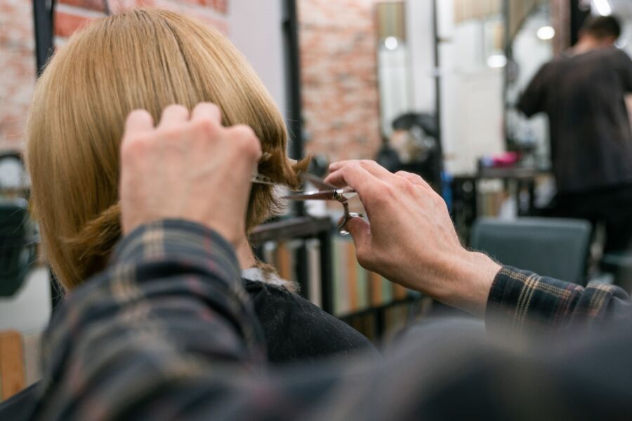 Peluquera cortando el pelo rubio de mujer en peluquería con tijeras y espejo.