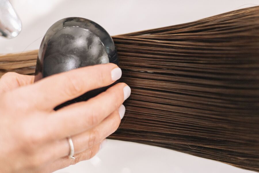 Primer plano de una mujer cepillando el cabello castaño largo con un cepillo negro, destacando el cuidado del cabello y el aseo.