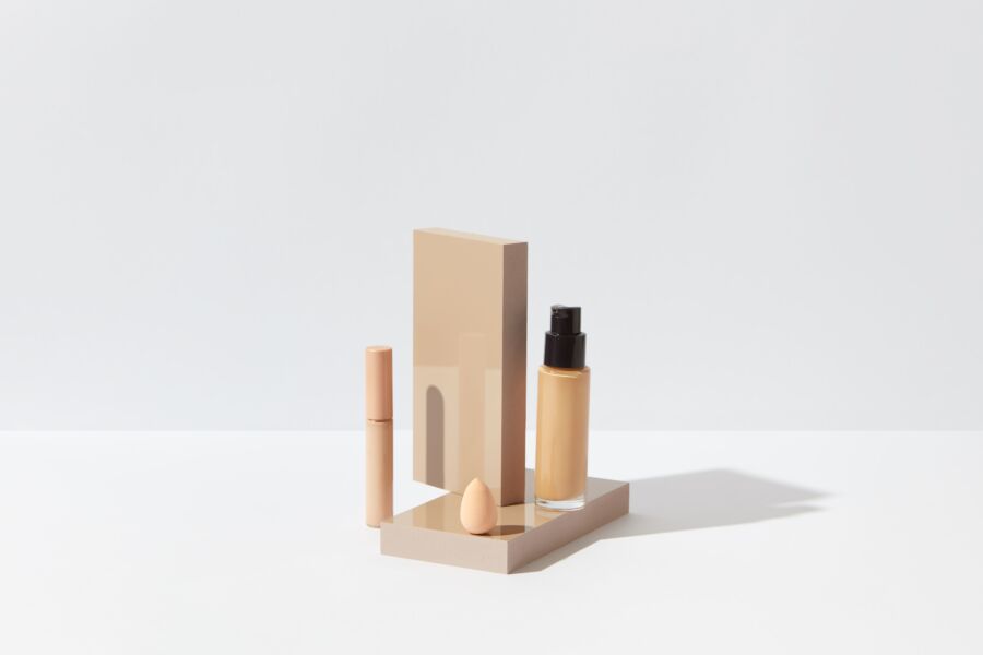 Elegante pantalla de base, corrector y esponja para una configuración de belleza limpia sobre una superficie blanca.