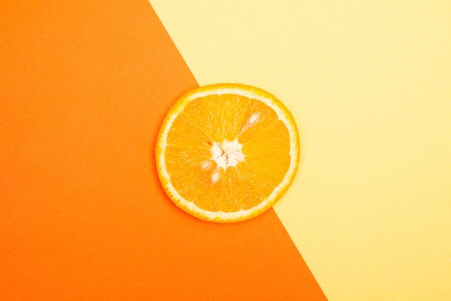 Rebanada de naranja brillante y jugosa sobre un fondo amarillo y naranja vibrante, perfecta para temas frescos y saludables.