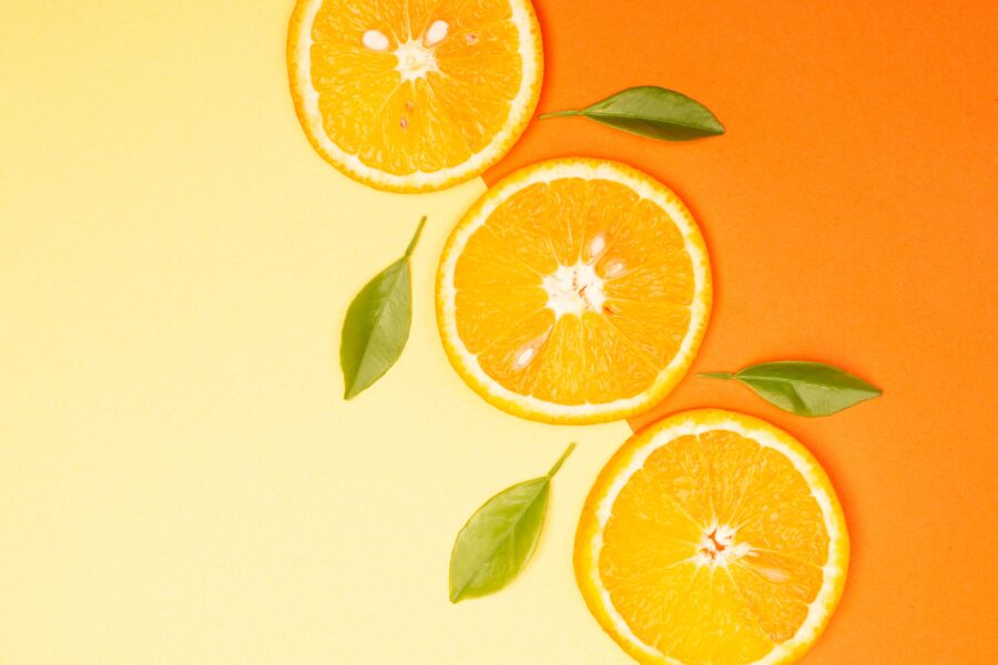 Primer plano de rodajas de naranja fresca con hojas verdes sobre un fondo degradado.