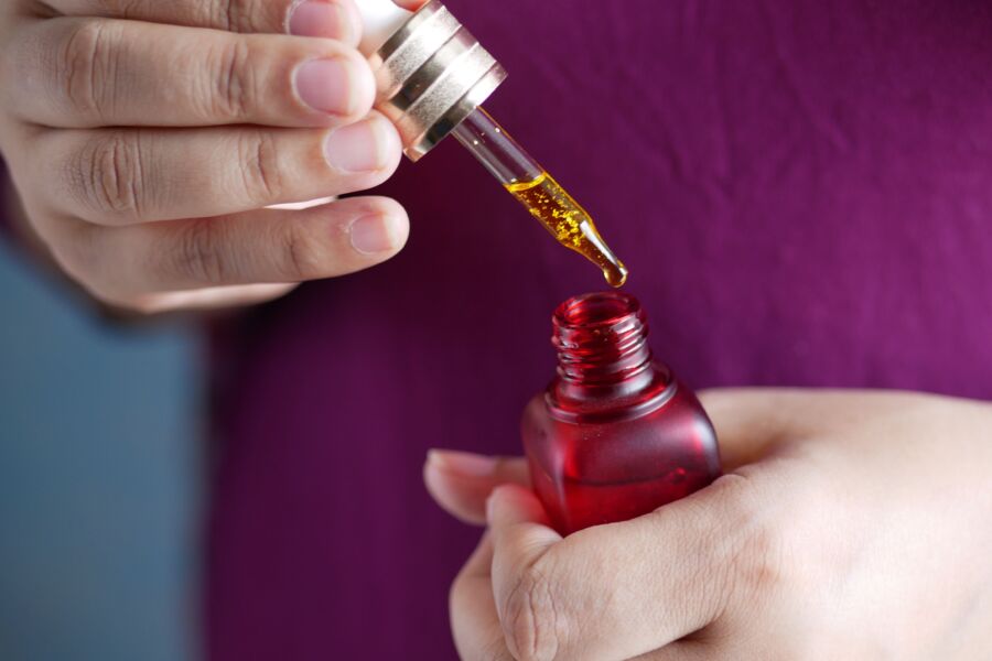Imagen detallada de las manos usando un cuentagotas con un frasco de vidrio rojo. Perfecto para el cuidado de la piel y temas de belleza.
