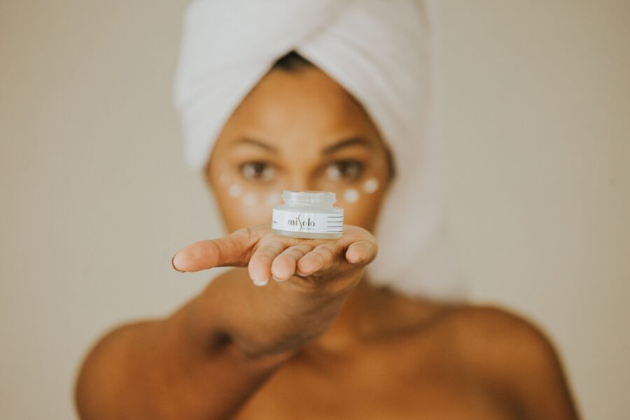 Mujer en topless sosteniendo una crema para el cuidado de la piel con puntos debajo de los ojos, promoviendo el cuidado de la belleza.