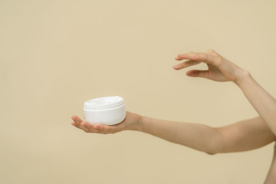Imagen minimalista de manos sosteniendo un frasco de cosméticos, enfatizando el cuidado de la piel y la belleza.