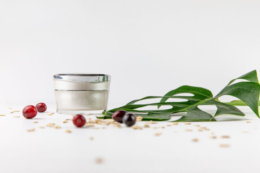 Primer plano de un tarro de crema cosmética con elementos naturales como hojas y bayas sobre fondo blanco.