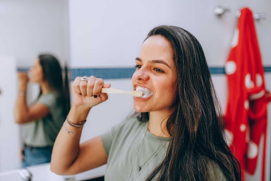 Mujer joven cepillándose los dientes con un cepillo de dientes en un baño moderno y luminoso. Centrarse en el cuidado y la higiene de la salud bucal.