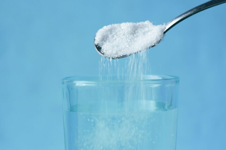 Verter azúcar en un vaso de agua sobre un fondo azul.