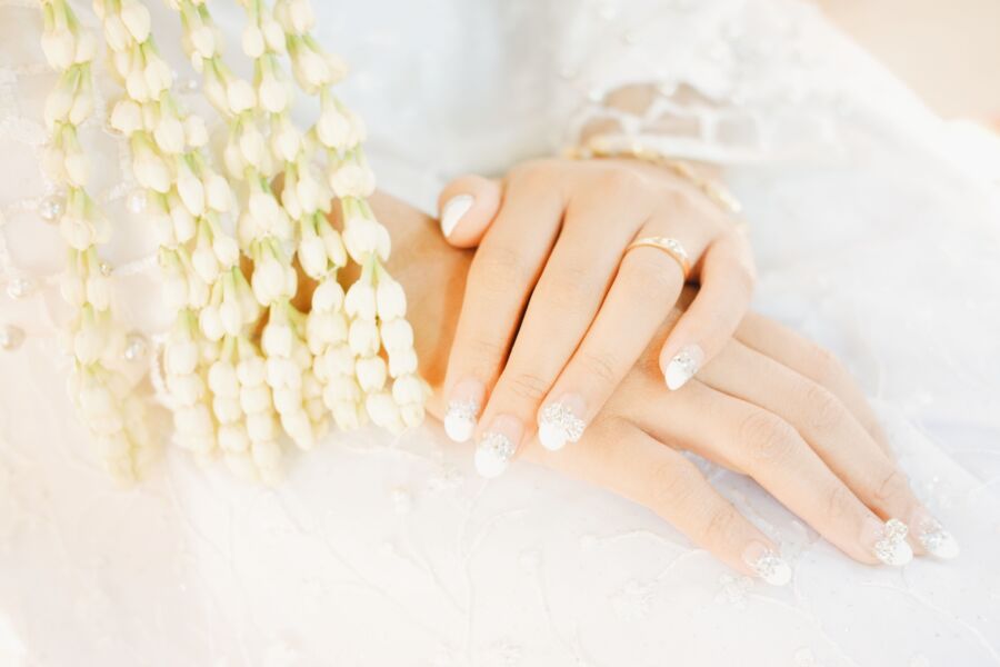 Primer plano de las manos de una novia con manicura intrincada y decoración floral, que simboliza la elegancia y la celebración.