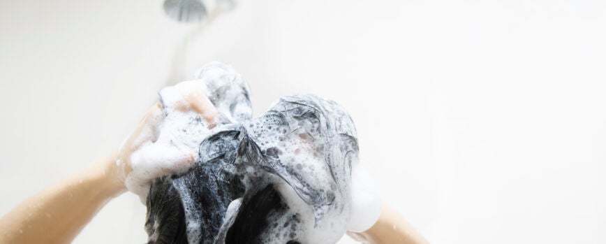 Señora que usa champú, lave / limpie el cabello en un baño con agua de rociador de ducha.