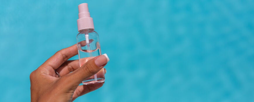 Manos sosteniendo una pequeña botella de líquido de aceite bronceador sobre piscina azul