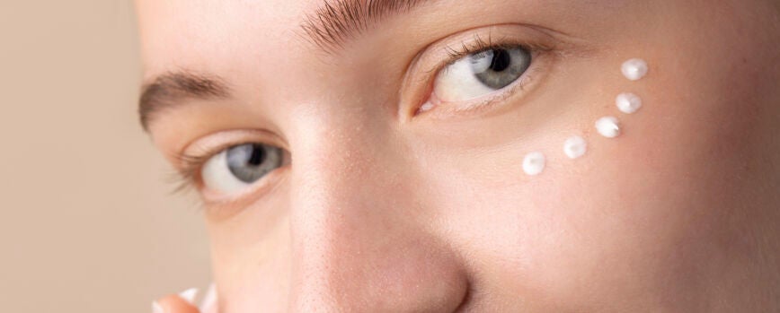 Modelo sonriente usando crema para los ojos de cerca