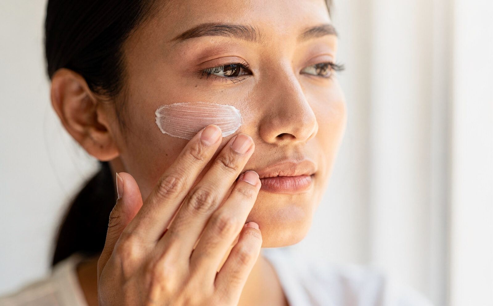 Persona genérica aplicándose crema solar en el rostro (proceso), sin mostrar la piel 'ya protegida/reparada'.