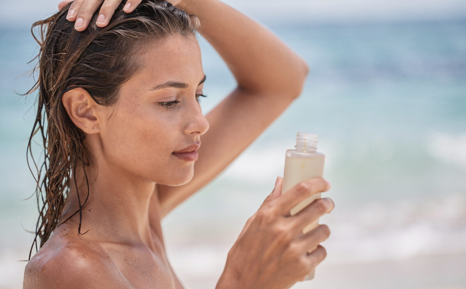 Persona genérica aplicándose aceite en el pelo antes de entrar al agua, envase visible, sin resultado final