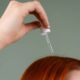 Primer plano de la mano aplicando suero capilar sobre el cabello rojo con un gotero.