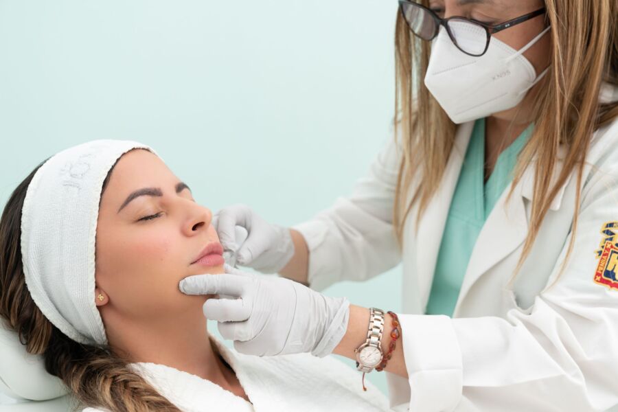 Médico que realiza un tratamiento cosmético en una mujer con los ojos cerrados en un entorno clínico.