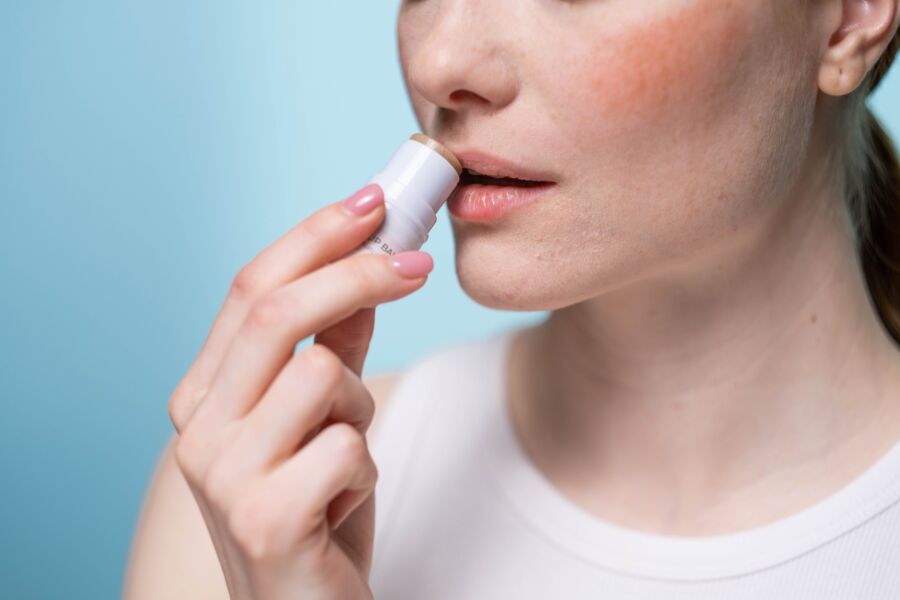 Una mujer aplicándose bálsamo labial en los labios, destacando la rutina de cuidado de la piel y el autocuidado.