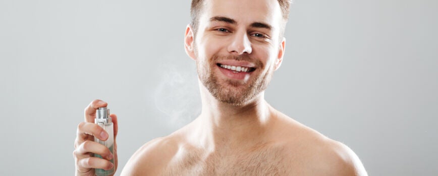 Retrato de un hombre semidesnudo sonriente rociando perfume