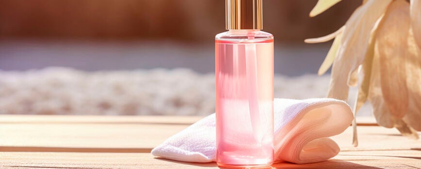 Vista cercana de la novia sexual con maquillaje y peinado con vestido de seda blanca y velo rociando perfume en su cuello y disfrutando del olor contra el fondo gris durante la mañana nupcial