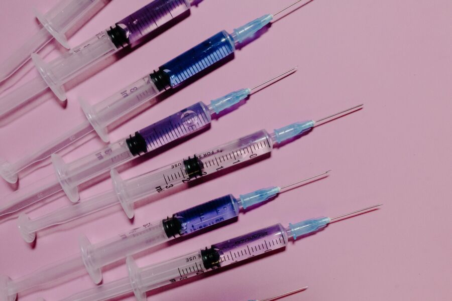 Varias jeringas con líquido azul sobre un fondo rosa, mostrando el equipo médico.