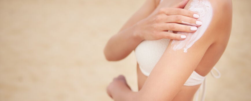 Joven y hermosa mujer aplicando crema solar en la playa