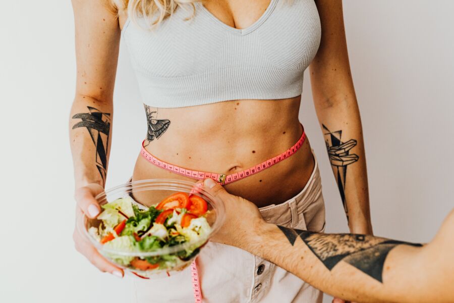 Mujer en forma midiendo la cintura mientras sostiene un ensaladero saludable