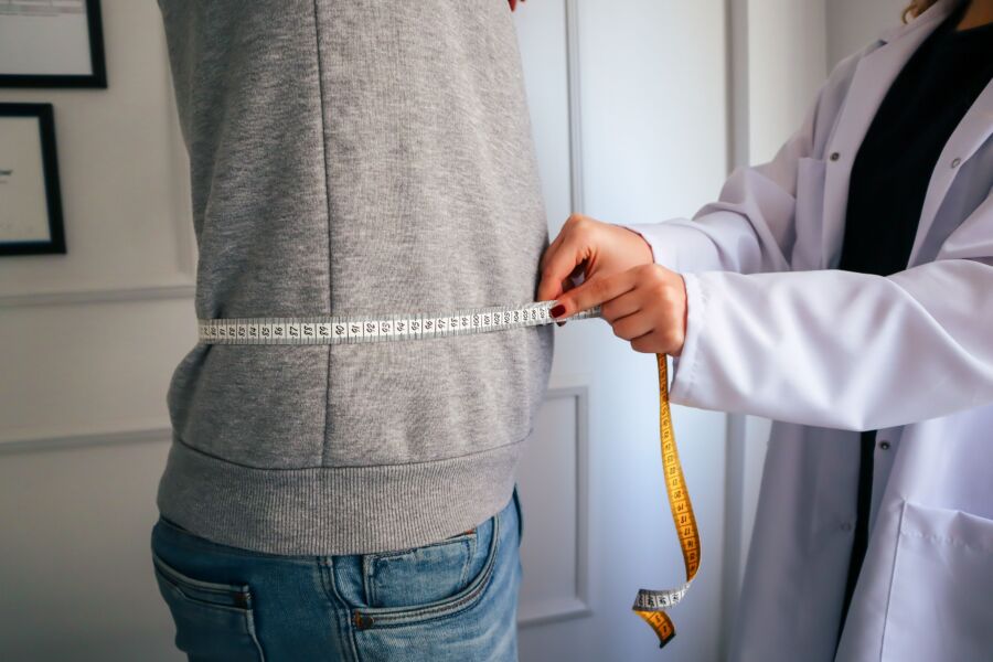Un nutricionista que mide la cintura de un paciente usando una cinta en un entorno clínico.