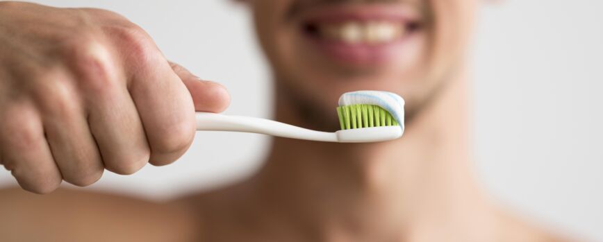 Vista frontal del hombre desenfocado con cepillo de dientes con pasta de dientes en él