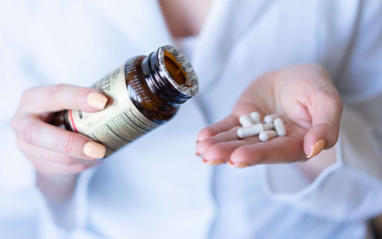 Un primer plano de las manos sosteniendo un frasco de medicamentos y píldoras, con un enfoque en la atención médica y el uso de medicamentos.