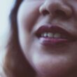 Primer plano de la cara de una mujer alegre irreconocible con cabello suelto oscuro con lápiz labial brillante y sonrisa dentada sobre fondo borroso a la luz del día