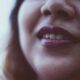 Primer plano de la cara de una mujer alegre irreconocible con cabello suelto oscuro con lápiz labial brillante y sonrisa dentada sobre fondo borroso a la luz del día