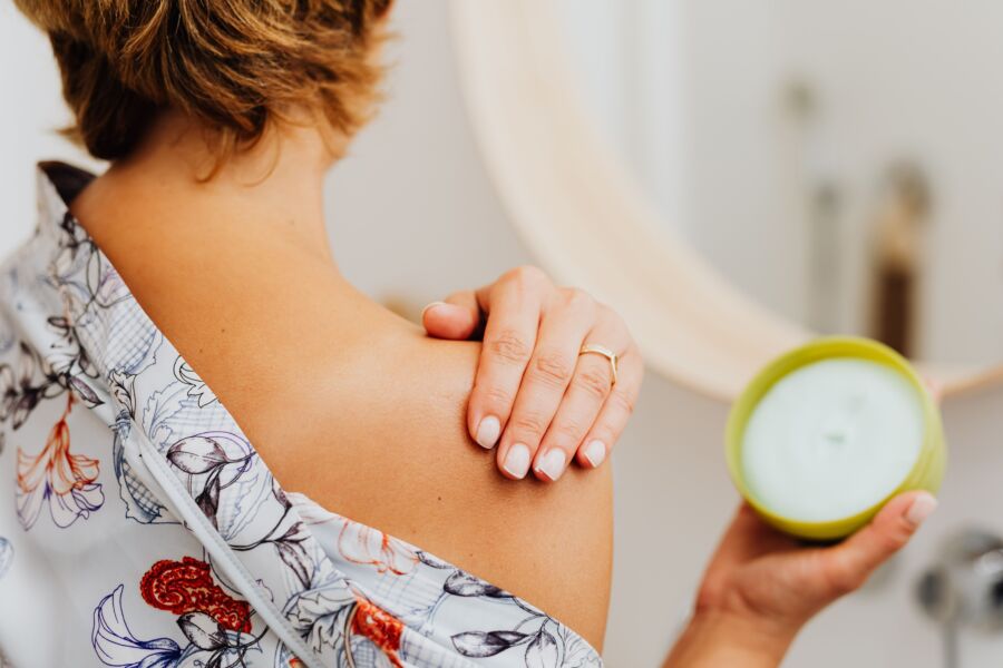 Primer plano de una mujer aplicándose crema corporal en el hombro en el baño.