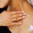 Una imagen en primer plano de una mujer que se aplica loción para el cuidado de la piel en el cuello con las manos bien cuidadas.