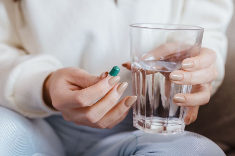 Mujer adulta con las manos sosteniendo una pastilla y un vaso de agua, lista para tomar la medicación.