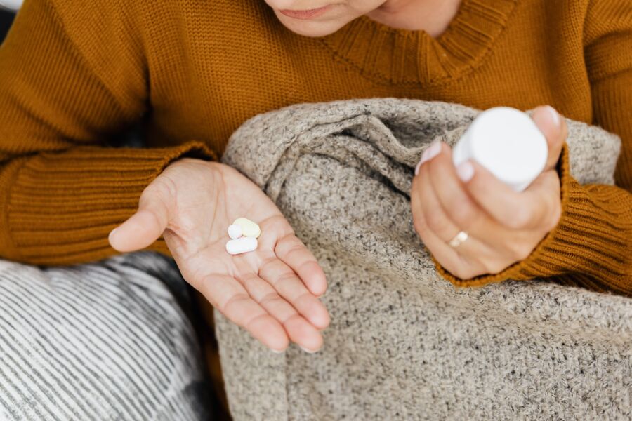 Primer plano de una mujer sosteniendo pastillas y un envase en un ambiente acogedor.