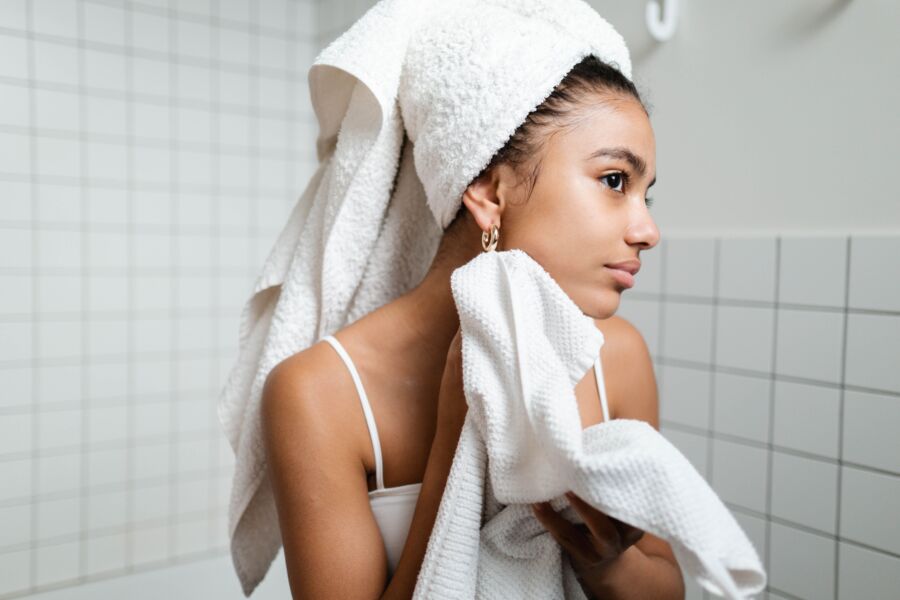 Mujer joven secándose la cara con una toalla durante la rutina de cuidado de la piel de la mañana en un baño moderno.