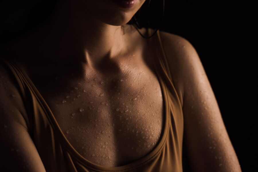 Primer plano de la piel húmeda de una mujer con gotas de agua, sobre un fondo oscuro.