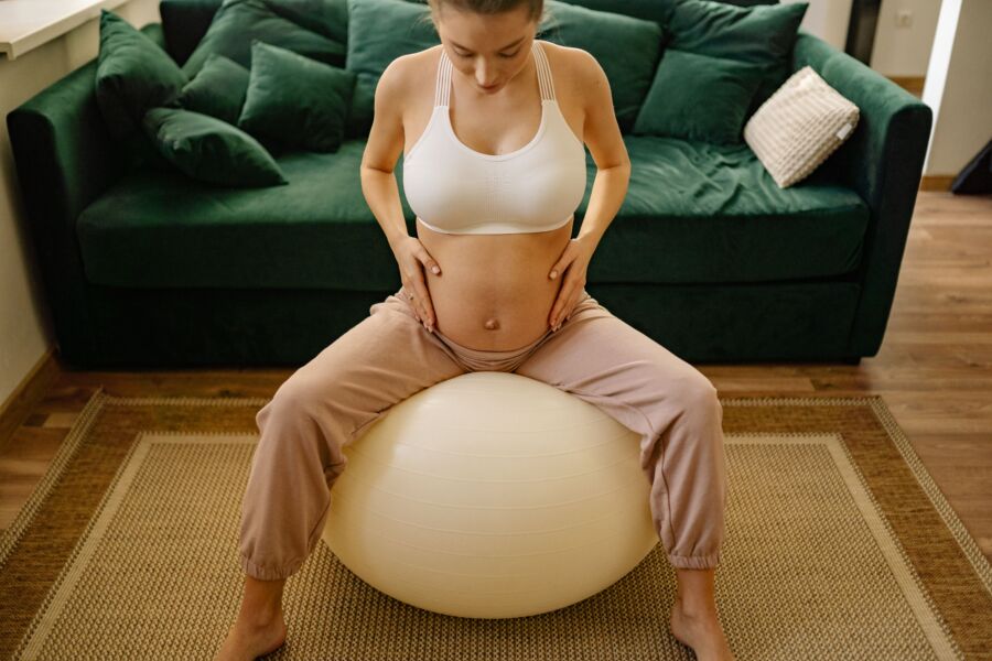 La futura madre practica ejercicios prenatales con una pelota de yoga en casa, enfatizando la condición física y el bienestar.