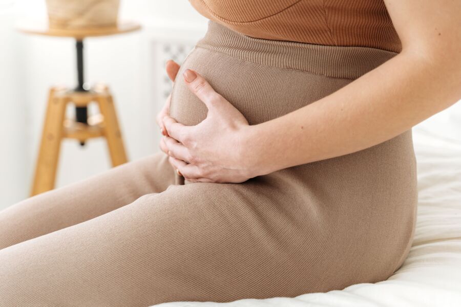 Un sereno primer plano de una mujer embarazada sosteniendo suavemente su vientre, capturado por la suave luz natural.